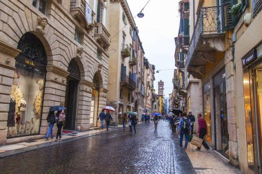 Verona, İtalya, 27 Nisan 2019 tarihinde. İnsanlar bir yağmur sırasında eski şehirde şehir sokak boyunca gitmek