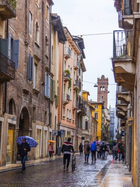 Verona, İtalya, 27 Nisan 2019 tarihinde. İnsanlar bir yağmur sırasında eski şehirde şehir sokak boyunca gitmek