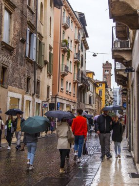 Verona, İtalya, 27 Nisan 2019 tarihinde. İnsanlar bir yağmur sırasında eski şehirde şehir sokak boyunca gitmek