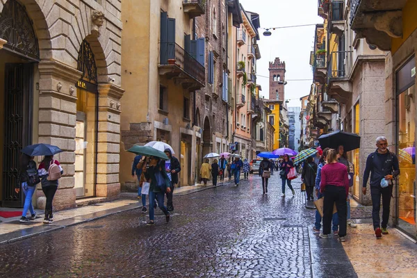 Verona, İtalya, 27 Nisan 2019 tarihinde. İnsanlar bir yağmur sırasında eski şehirde şehir sokak boyunca gitmek