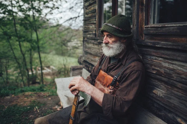 Portrait of old bearded forester with axe near wooden hut