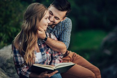 Kayanın üzerinde oturan ve kitap okuma genç çift