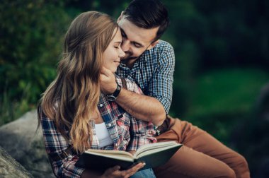 Kayanın üzerinde oturan ve kitap okuma genç çift