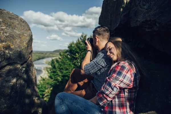 Woman relaxing and man taking photos of mountain landscape on digital camera