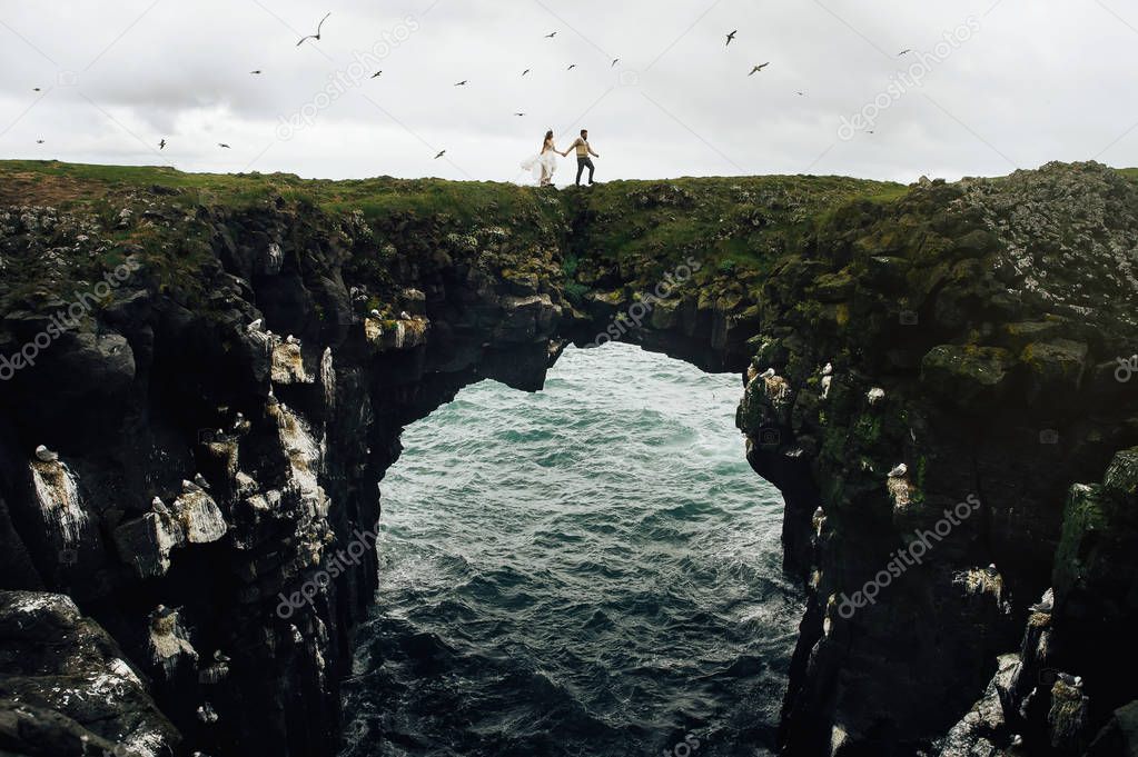 New wedded couple walking on natural stone gate over nordic sea