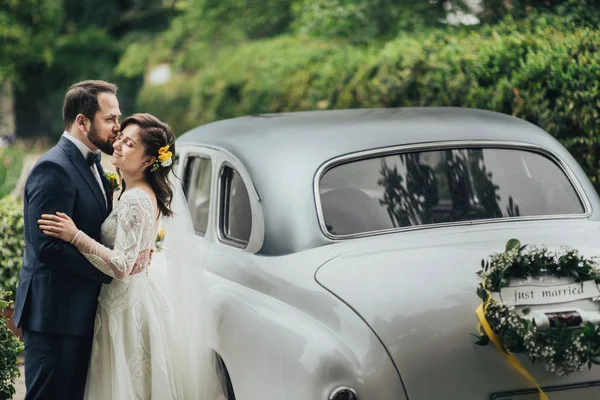 Glückliches Luxus-Hochzeitspaar küsst und umarmt sich in der Nähe von Retro-Auto. — Stockfoto