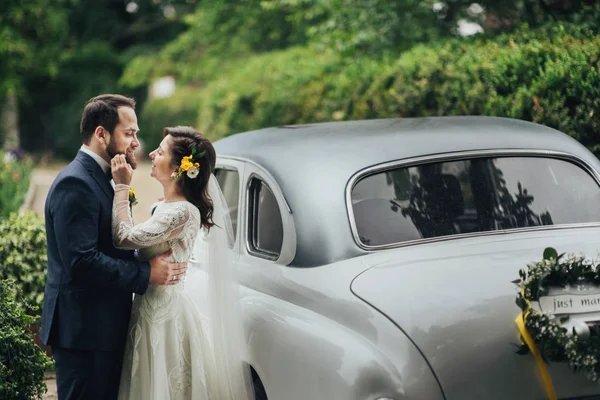 Feliz pareja de boda de lujo besando y abrazando cerca de coche retro . — Foto de Stock