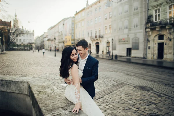 街の通りでポーズレースのウェディングドレスで幸せな新郎とエレガントな花嫁 — ストック写真