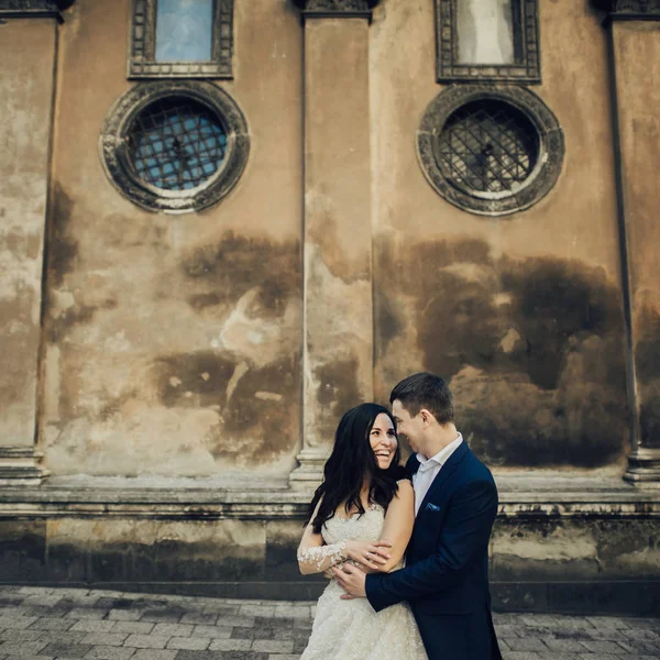 陽気な花嫁と新郎はヴィンテージみすぼらしい建物の壁の背景に抱きしめる — ストック写真