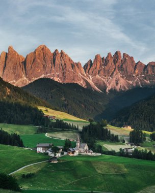 Beautiful village in the Alps. Santa Magdalen on Dolomites Background. Sunset in the mountains in Italy. Red peaks of mountains. clipart