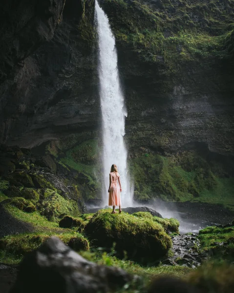 Menina jovem e bonita em vestido rosa suave olhando para a cachoeira na Islândia. Islândia cachoeira natureza viagens paisagem em islandês natureza fundo . — Fotografia de Stock