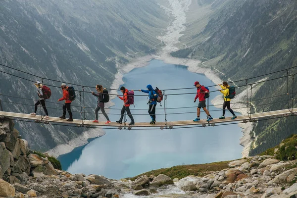 Team of travelers with a backpack in the mountains. A group of travelers crosses a suspension bridge against the backdrop of a mountain and a glacier. Travel and active life concept. Adventure trip.