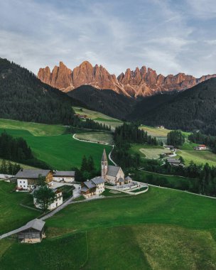Beautiful village in the Alps. Santa Magdalen on Dolomites Background. Sunset in the mountains in Italy. Red peaks of mountains. Top view by drone.