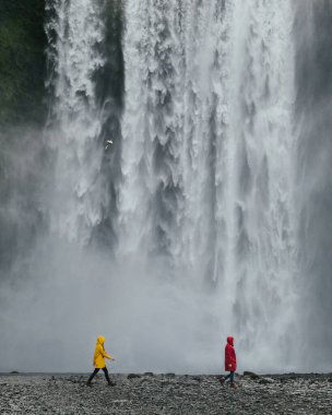İzlanda 'da büyük bir şelale olan Skogafoss' un arka planında renkli yağmurluklu gezginler. Destansı manzara seyahati aktif turizm ve macera içeriği.