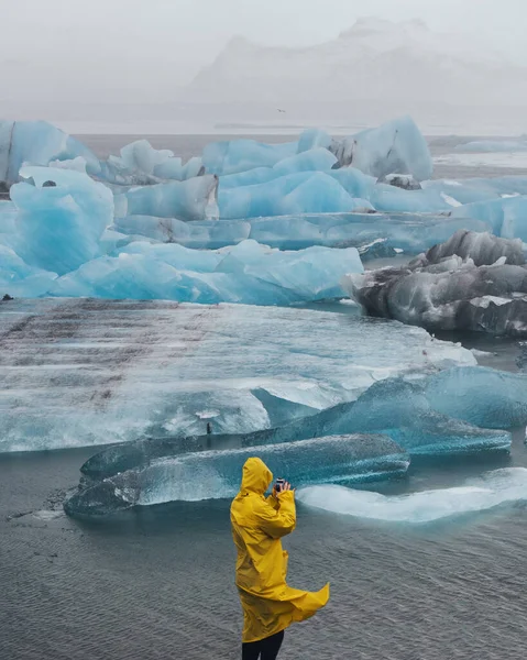 北極の大きな青い氷山の背景にいる人 アイスランドの氷河を背景に黄色のレインコートを着た旅行者 男との壮大な風景 旅と冒険のコンセプト ストック写真