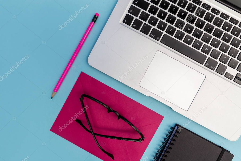 Laptop with eyeglasses, notebooks and pencil on bright blue background