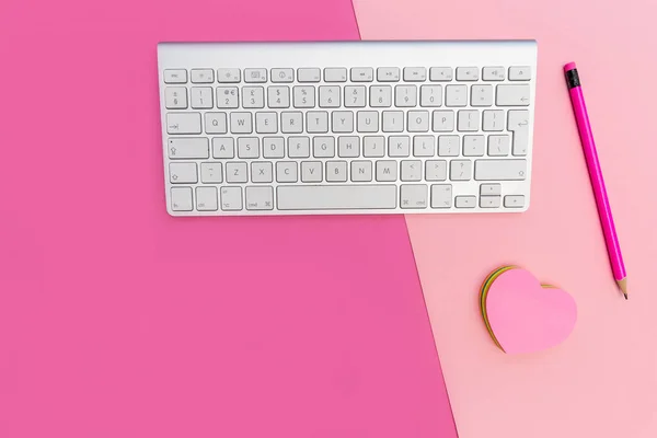 Minimal office workplace view. Computer keyboard on bright pink background