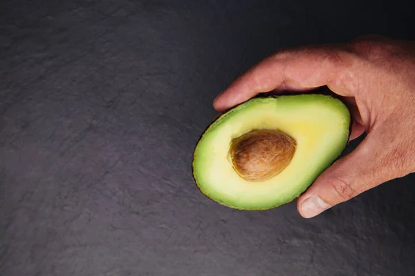 Handen Håller Avokado Hälften Mörk Bakgrund — Stockfoto