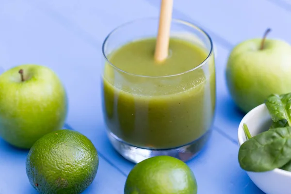 Healthy green smoothie drink with straw on blue table background