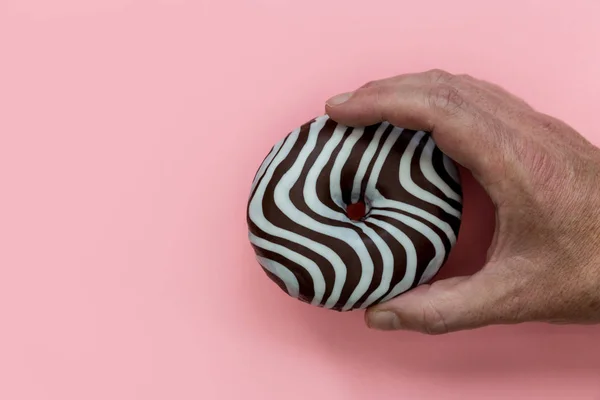 Mannelijke Hand Met Gestreepte Chocolade Donut Roze Achtergrond — Stockfoto