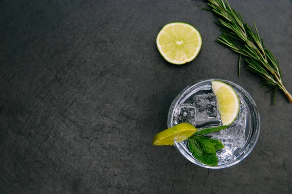Cin tonik kokteyl içmek koyu arka plan üzerinde buz cam yeşil limonlu