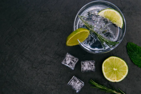 Cin tonik kokteyl içmek koyu arka plan üzerinde buz cam yeşil limonlu