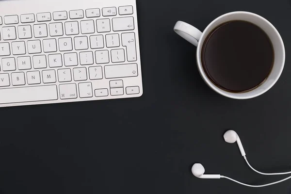 Minimal office desk computer keyboard coffee music earphones on dark background