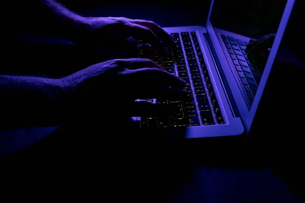 Man typing on laptop computer keyboard at night online cyber crime hacker concept