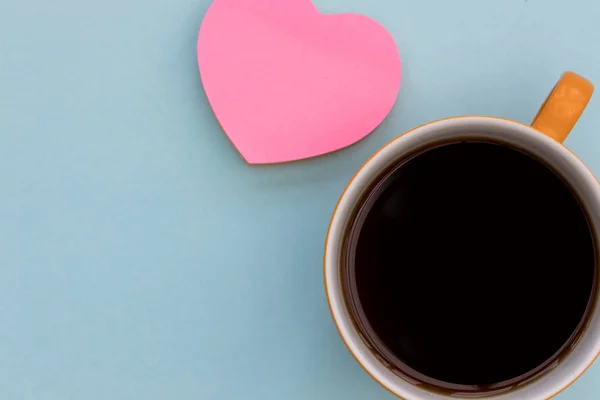 Coffee cup and pink love heart top view on blue color minimal background