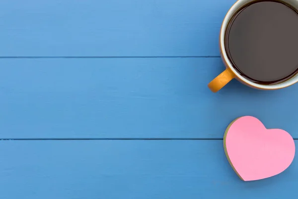 青い木製のテーブルのミニマルな背景にコーヒーカップとピンクの愛のハートトップビュー — ストック写真