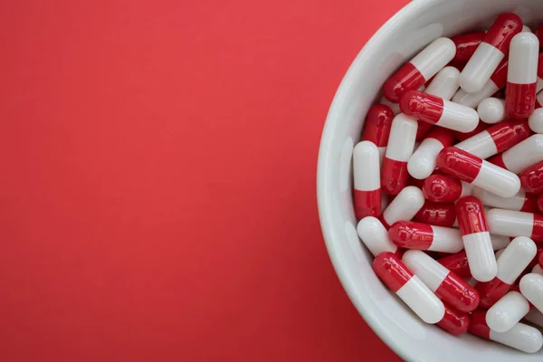 Чаша с таблетками капсулы на красном фоне — стоковое фото
