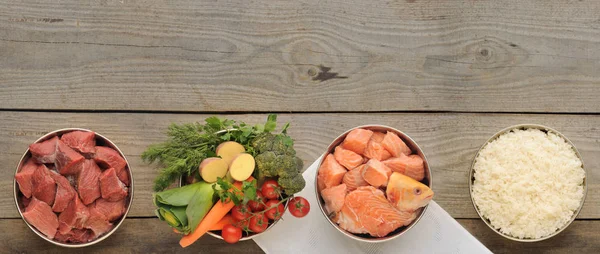 Natural ingredients for dog food in four bowls on old wooden background