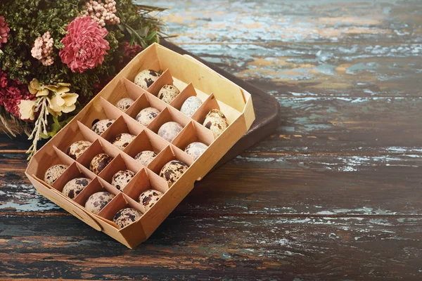 Open eco-friendly wooden box with quail eggs near dry flowers on rough dyed wooden background. Eggs For Easter.