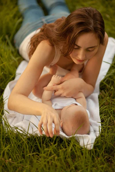 美丽的女人与可爱的婴儿躺在绿色的草地上 幸福家庭 — 图库照片