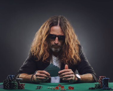 Uzun saçlı yakışıklı adam bir casino poker oynamaya. Stüdyo konsepti gri arka plan üzerine