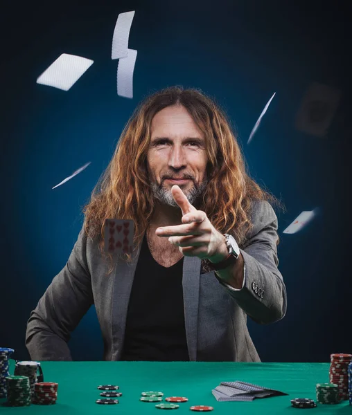髪の長いハンサムな男がカジノでポーカーをプレイします 青色の背景のスタジオ コンセプト — ストック写真