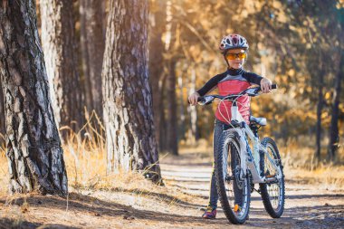 güneşli ormandaki bir bisikletle evlat. mutlu kız açık havada kask içinde Bisiklete binme