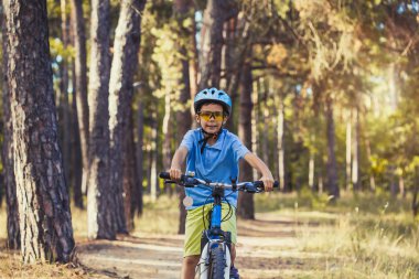 Güneşli ormandaki bir bisikletle komik çocuk. mutlu çocuk açık havada kask içinde Bisiklete binme