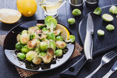Ev yapımı kavrulmuş Brussel lahanası ile Parmesan peyniri, limon, tuz, biber siyah ahşap bir masa üzerinde.