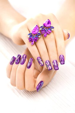 Beyaz ahşap masa üzerinde Küpeli güzel mor manikür.