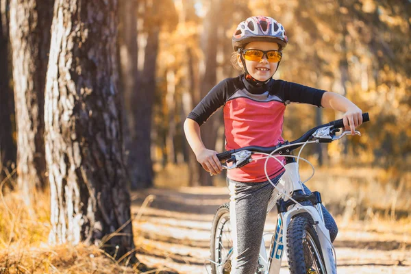 孩子在阳光明媚的森林里骑自行车 快乐的女孩骑头盔在户外骑自行车 — 图库照片