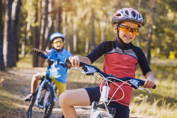 孩子们在阳光明媚的森林里骑着自行车 快乐的孩子们戴着头盔在户外骑车 — 图库照片