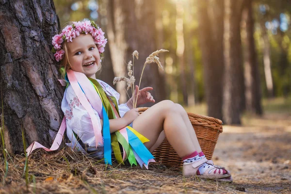 リボンと花輪の少女は夏の森でのツリーの下に座っています ウクライナの民族衣装 — ストック写真