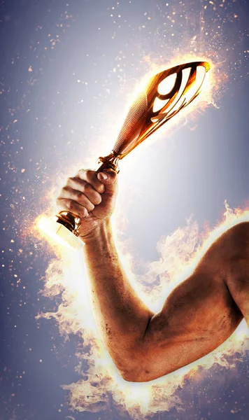 Man\'s hand in a fire is holding gold cup on a dark background. Winner in a competition.