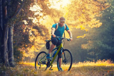 Mutlu sakallı adam dağ bisikletiyle güneşli ormanda bisiklet sürüyor. Macera seyahati.