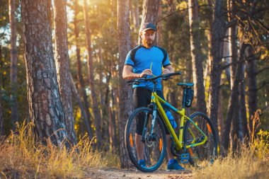 Mutlu sakallı adam dağ bisikletiyle güneşli ormanda bisiklet sürüyor. Macera seyahati.