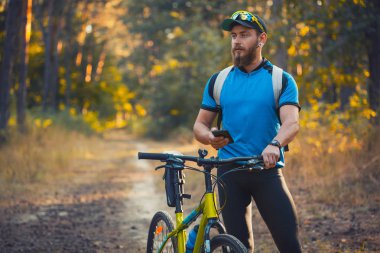 Mutlu sakallı adam dağ bisikletiyle güneşli ormanda bisiklet sürüyor. Macera seyahati.