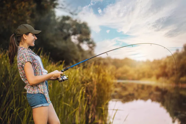 Cute woman is fishing with rod on the summer lake