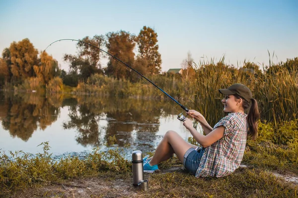 Happy woman is fishing with rod on the summer lake