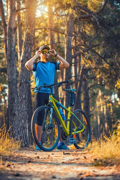 Happy bearded man cyclist rides in the sunny forest on a mountain bike. Adventure travel.